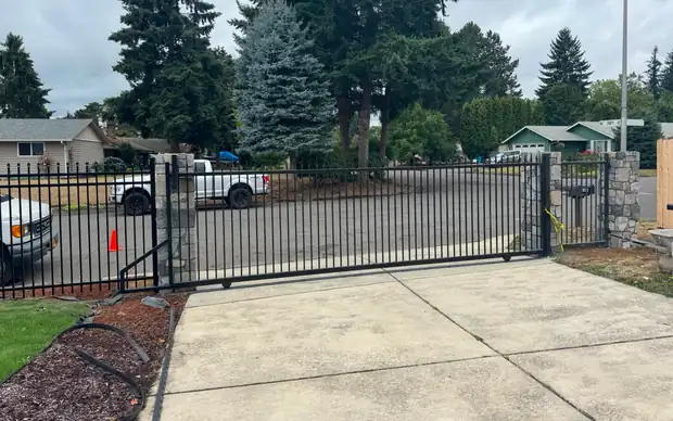 Black iron cantilever slide gate closed across driveway with stone columns, cloudy day — Interstate Gate Repair