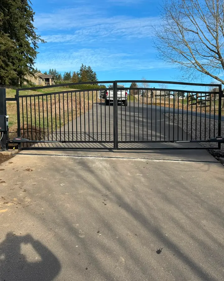 Closed dual-swing black metal driveway gate with LiftMaster operators, blue sky — Interstate Gate Repair