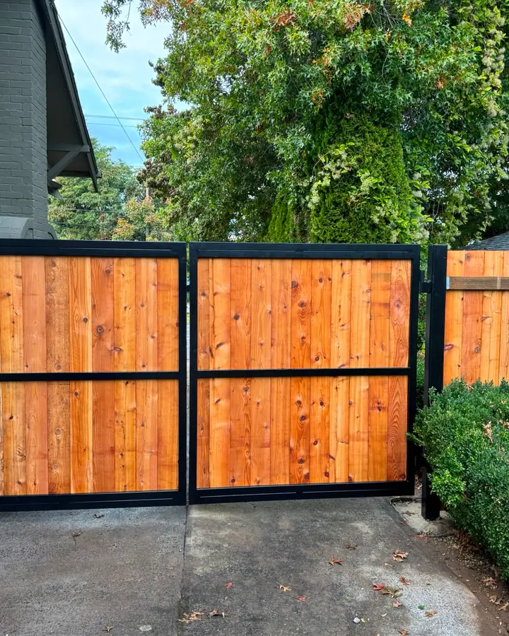 Two-panel cedar swing gate with black steel frames flanked by hedges — Interstate Gate Repair