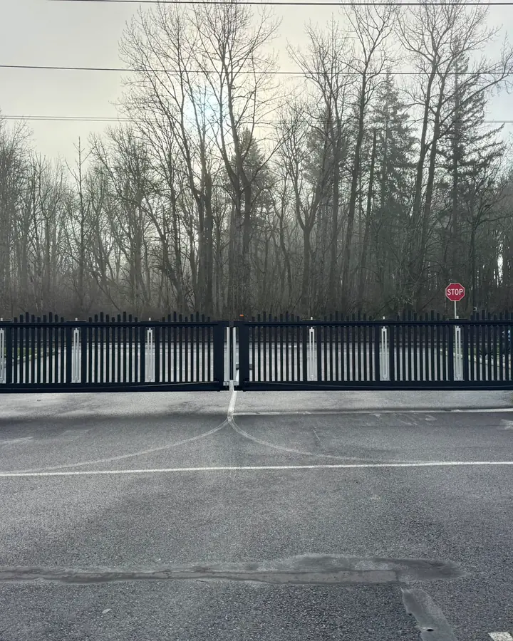 Wide view of black bi-parting slide gate closed across driveway with STOP sign — Interstate Gate Repair