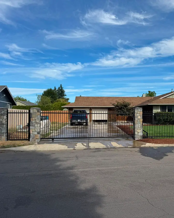 Front street view of ranch home with black iron fence, slide gate and stone pillars — Interstate Gate Repair