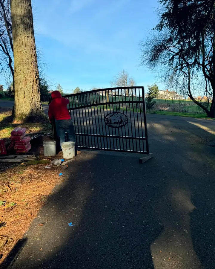 Black metal driveway gate with mountain elk emblem staged at rural entrance — Interstate Gate Repair